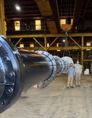 Large black vertical pump extending across the PumpRite shop with two people standing beside it