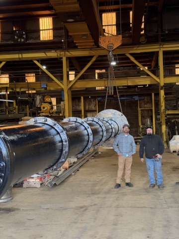 Vertical pump assembly from the opposite angle with an overhead crane and two people beside the pump